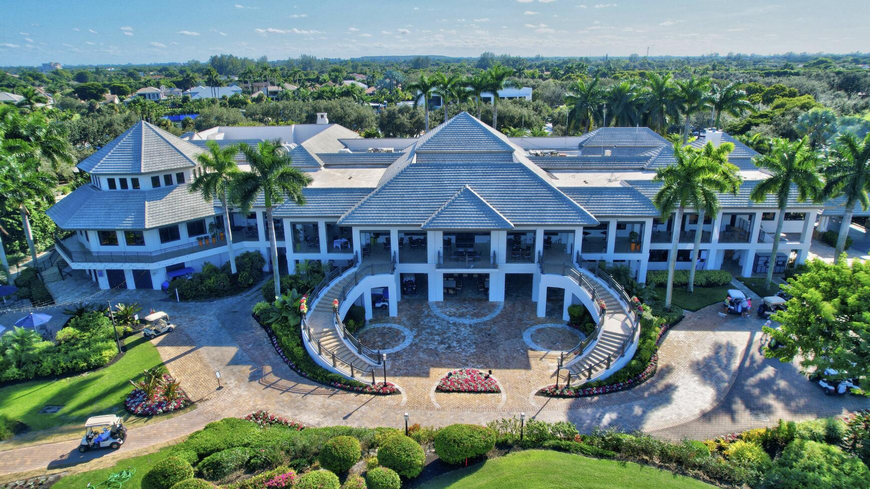 Aerial view of a white residential building with tiled roofs, palms, and a circular landscaped drive.