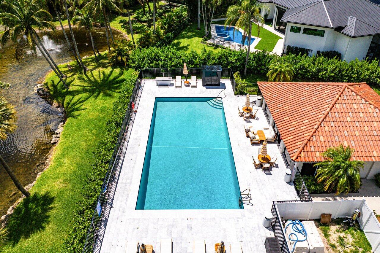 Aerial view of a rectangular pool and furnished patio beside a palm-lined canal.