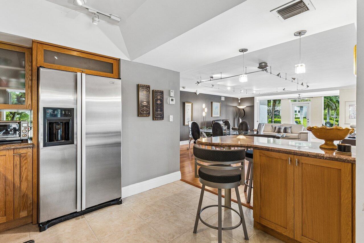 Open-plan kitchen with wood cabinetry, stainless steel refrigerator, and breakfast bar overlooking the dining and living areas.