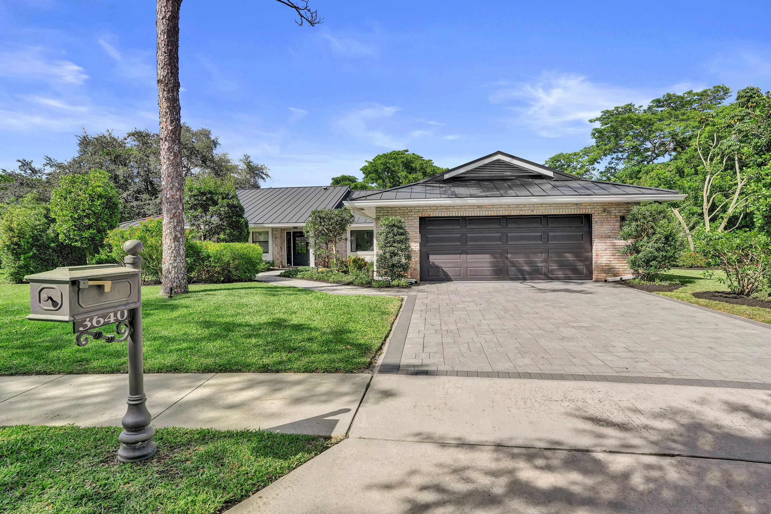 Single-story brick home with a dark metal roof, two-car garage, and landscaped front yard.