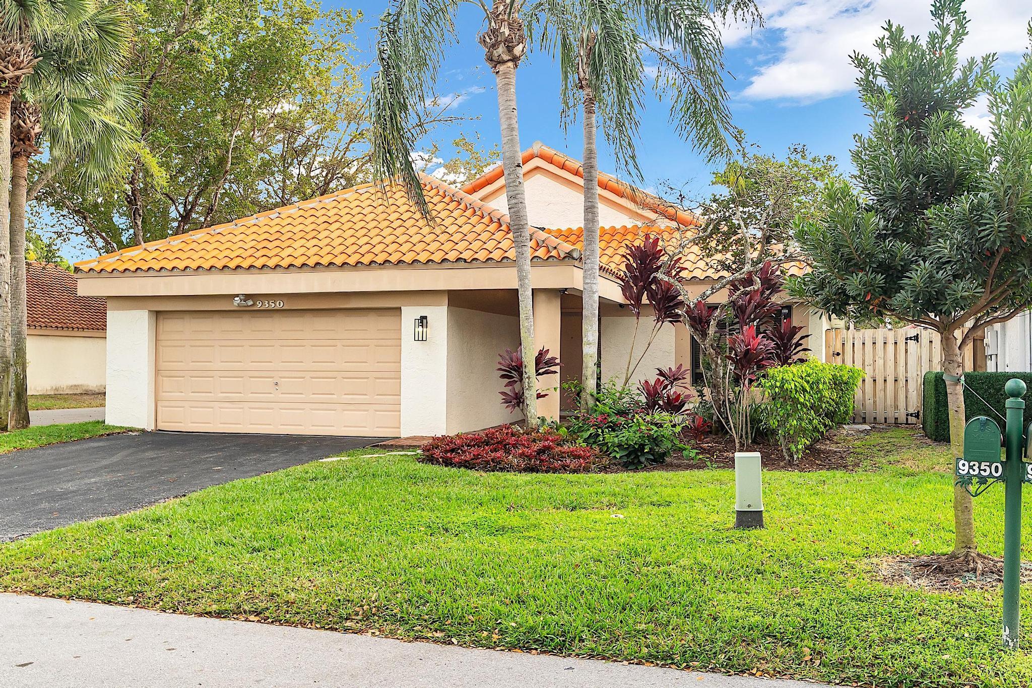 Home exterior with terracotta tile roof, double garage, tropical landscaping, and lawn.