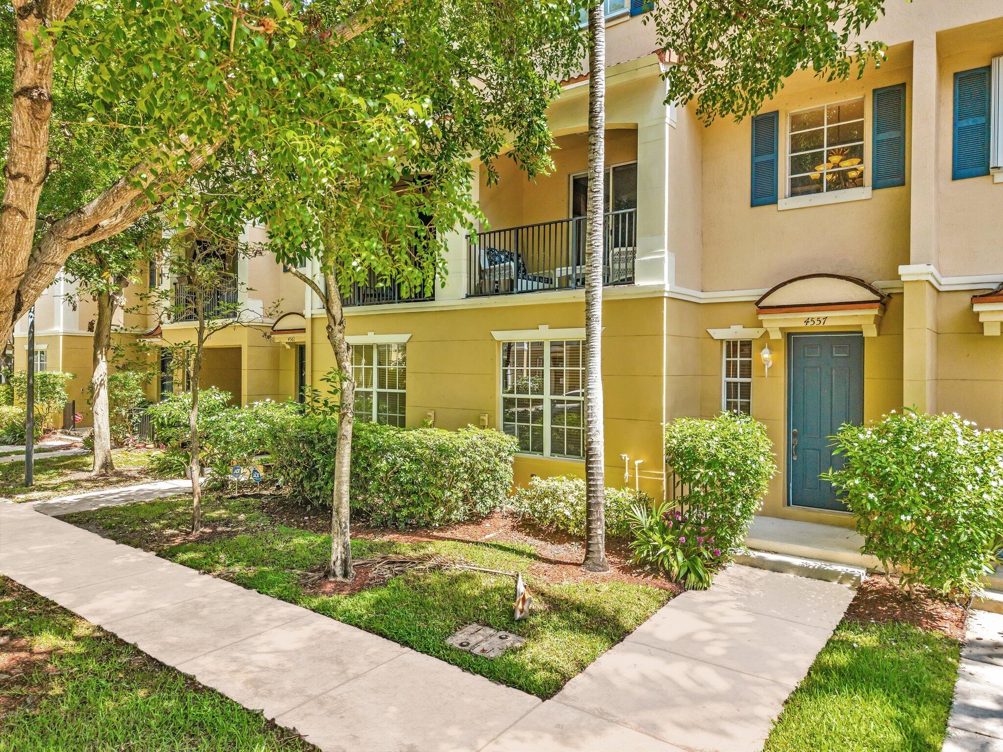 Yellow residential building with blue entry door, balconies, and leafy landscaping.