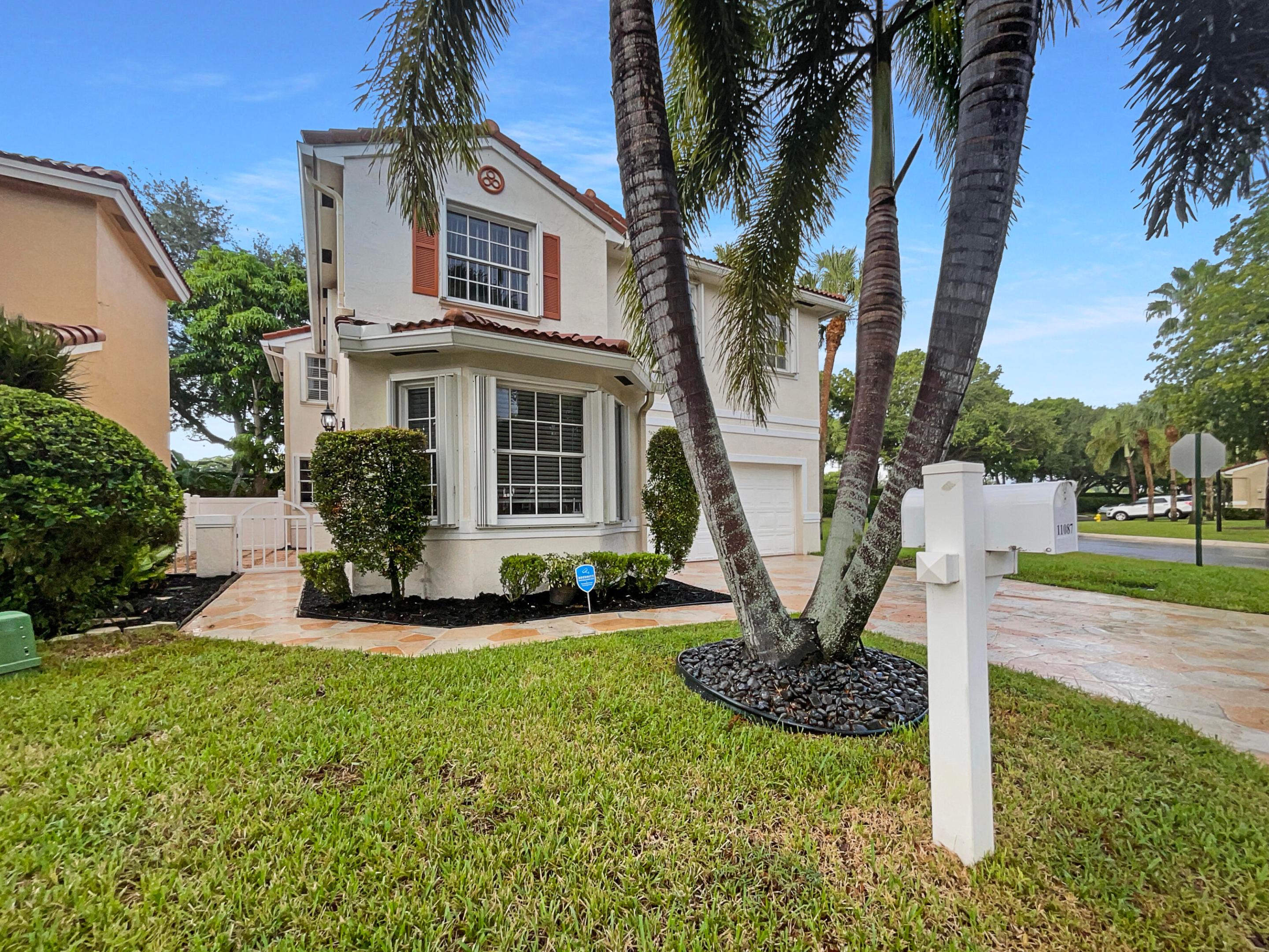 Two-story cream home with terracotta roof tiles, palm trees, and a white mailbox marked 11087.
