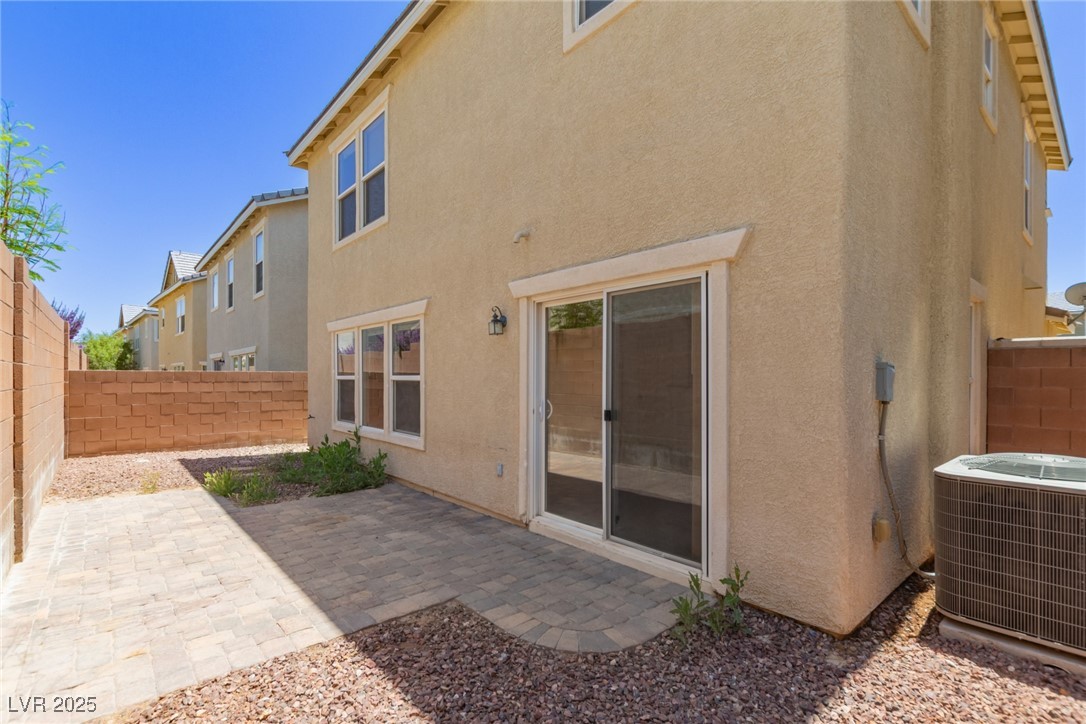 Two-story beige stucco home with a paver patio, gravel yard, and sliding glass door.