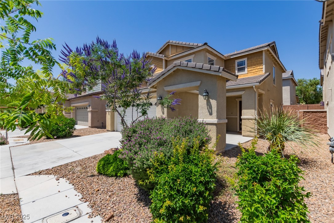 Two-story tan stucco home with an attached garage, covered entry, and flowering desert landscaping.