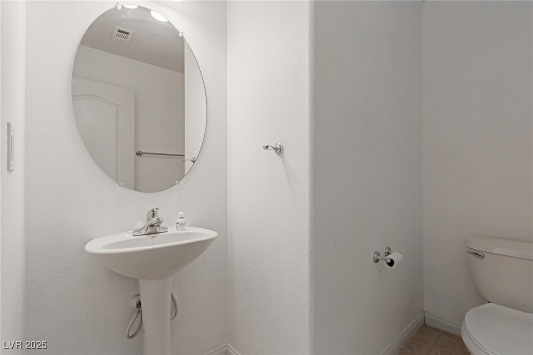 Small bathroom with a pedestal sink, oval mirror, and partially visible toilet.