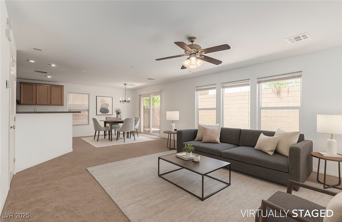 Virtually staged open-plan living and dining room with gray sofa, ceiling fan, and kitchen.
