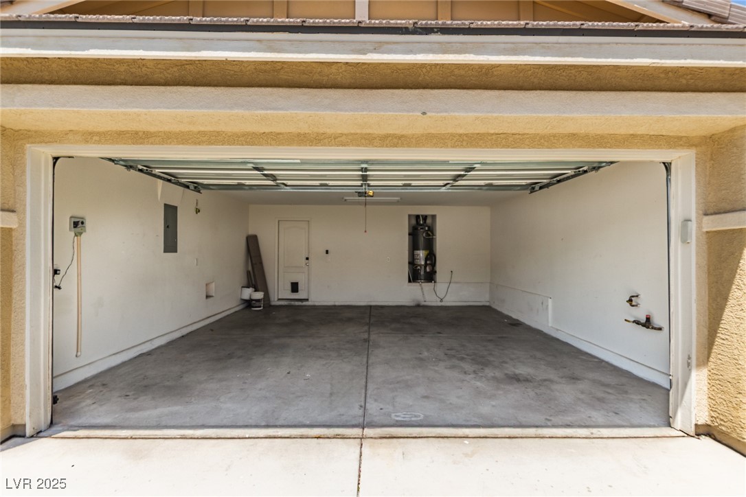 Open garage with an empty concrete floor, interior door, and water heater.