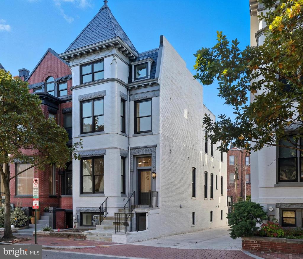 White brick townhouse with a steep slate roof and bay windows beside red brick rowhouses.