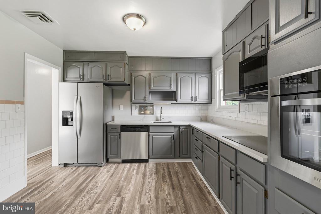 Kitchen with gray cabinets, stainless steel appliances, white countertops, and wood-look flooring.