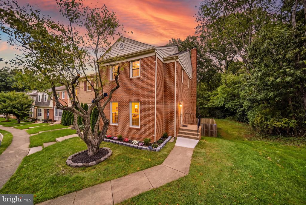 Two-story brick townhouse with a landscaped front yard and sidewalk beneath a pink-orange sunset sky.