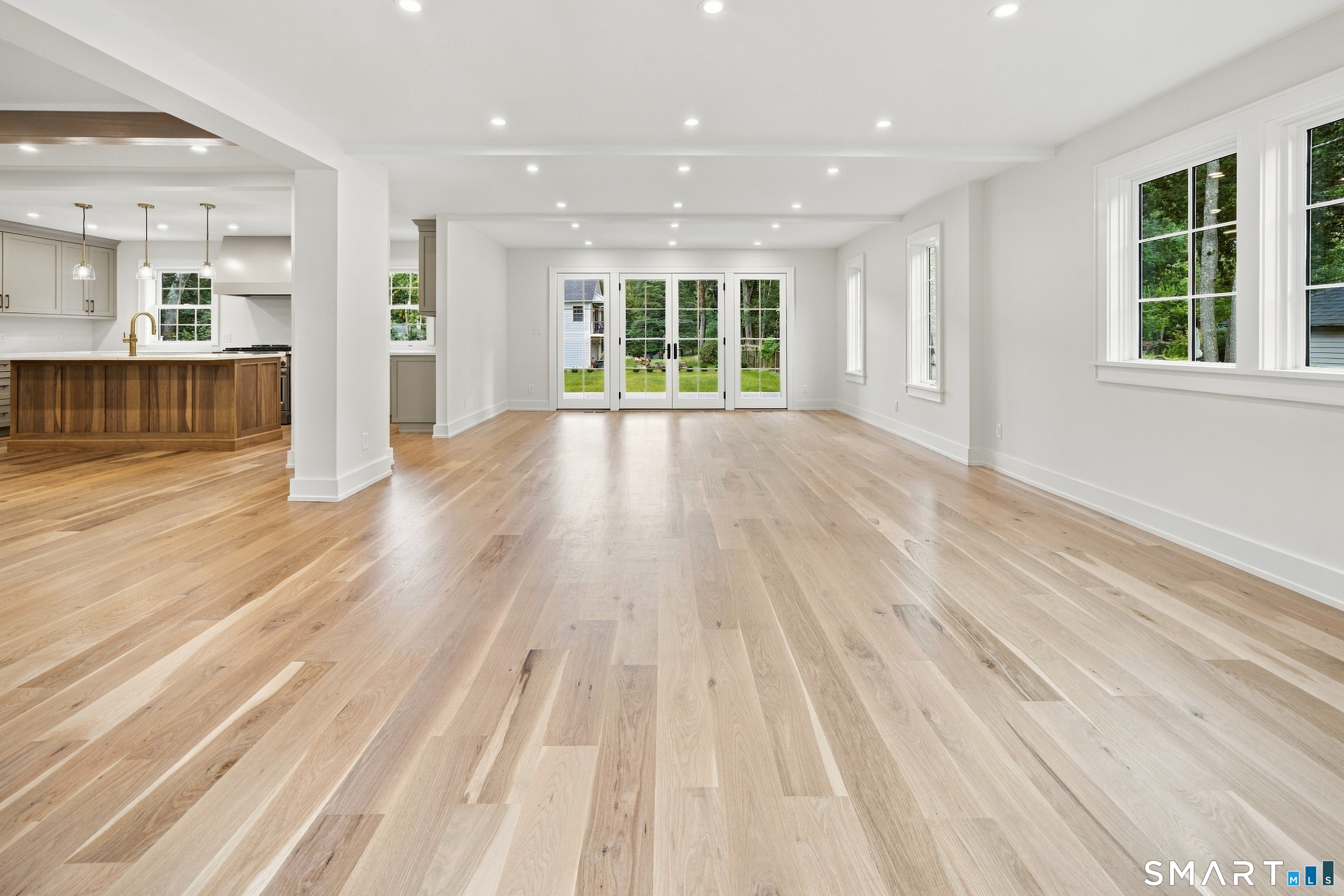 Vacant open-plan living room with wide hardwood floors, a wood-front kitchen island, and French doors to the yard.