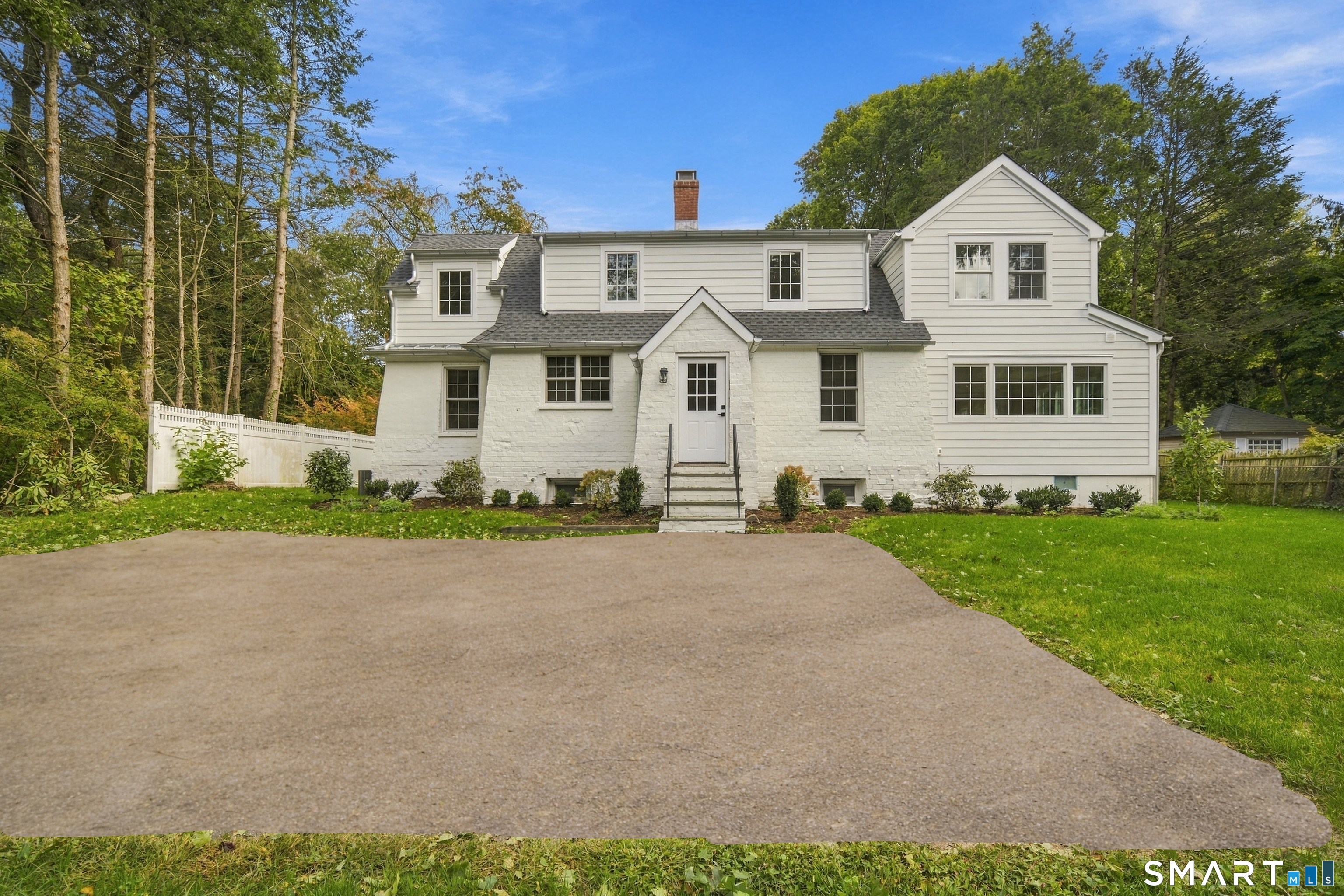White two-story house with a stone facade, central entry steps, and a broad paved foreground.