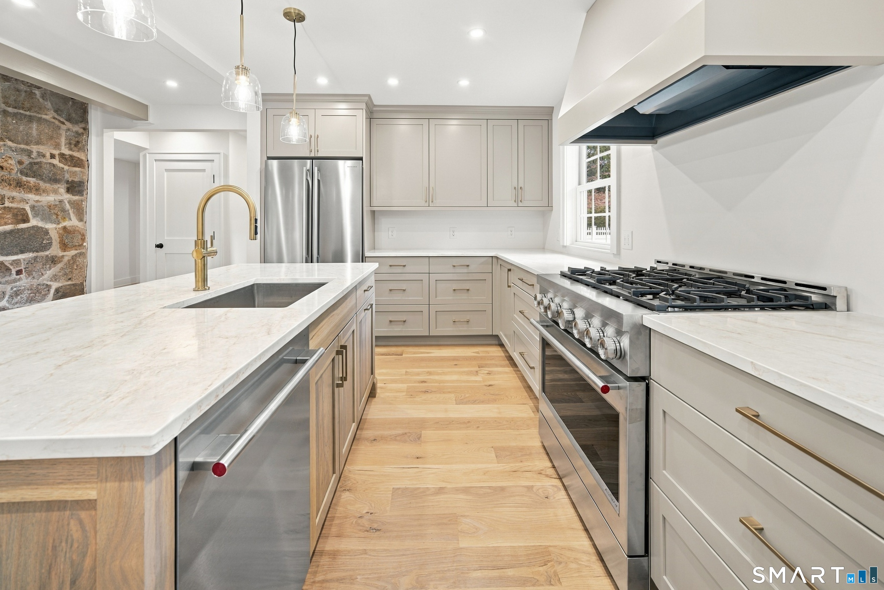 Renovated kitchen with a large island, brass faucet, stainless steel range, and white cabinetry.