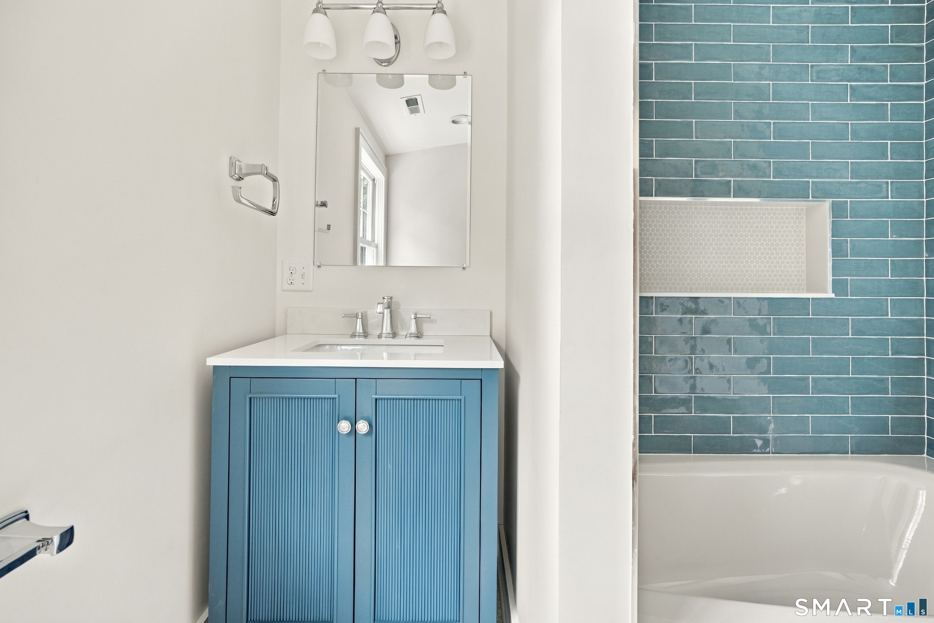 Bathroom with a blue fluted vanity and bathtub against blue subway tile.