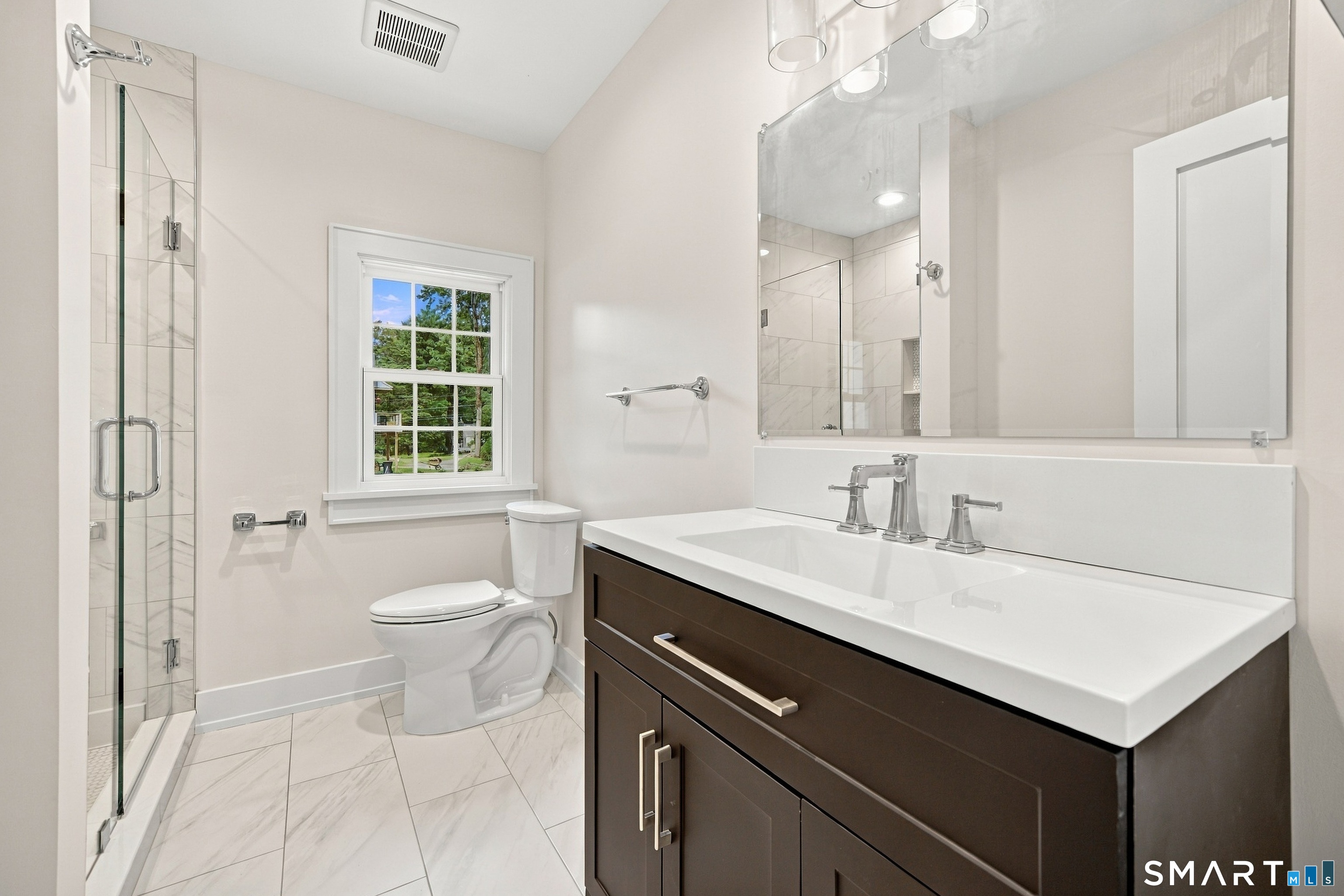 Modern bathroom with a glass walk-in shower, marble-look tile, and dark wood vanity.