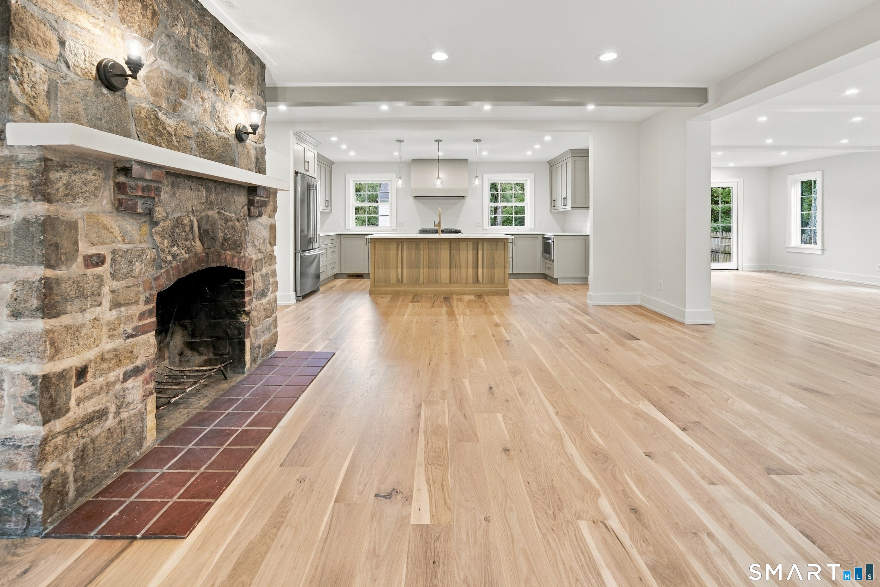 Open kitchen and living area with a wood island, pale floors, and a large stone fireplace.
