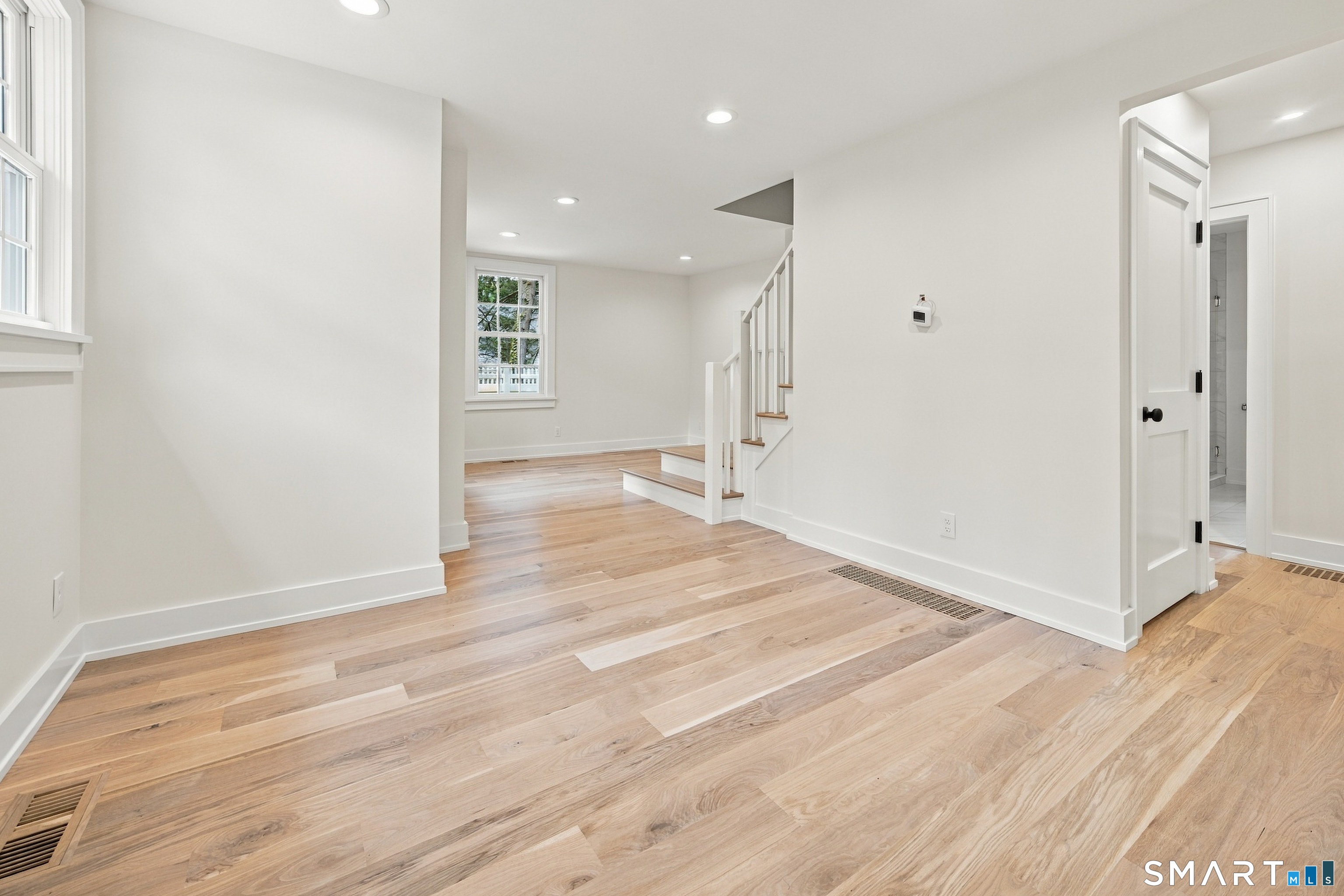 Bright empty entry with light hardwood floors, windows, and a staircase.