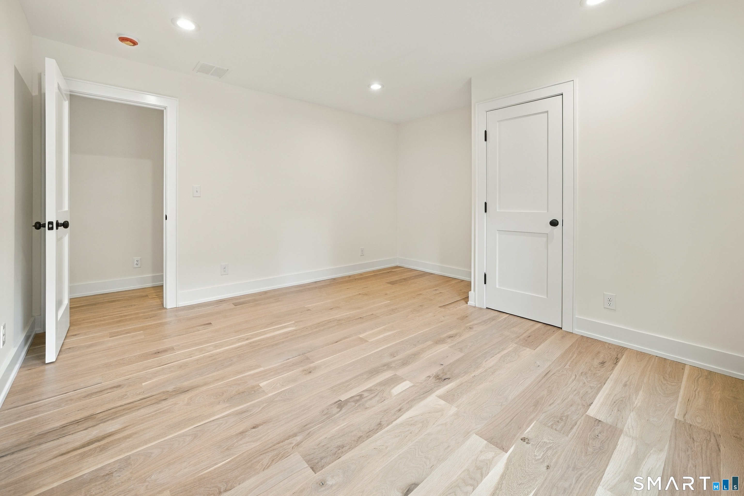 Empty room with light wood floors, white walls, recessed lights, and two paneled doors.
