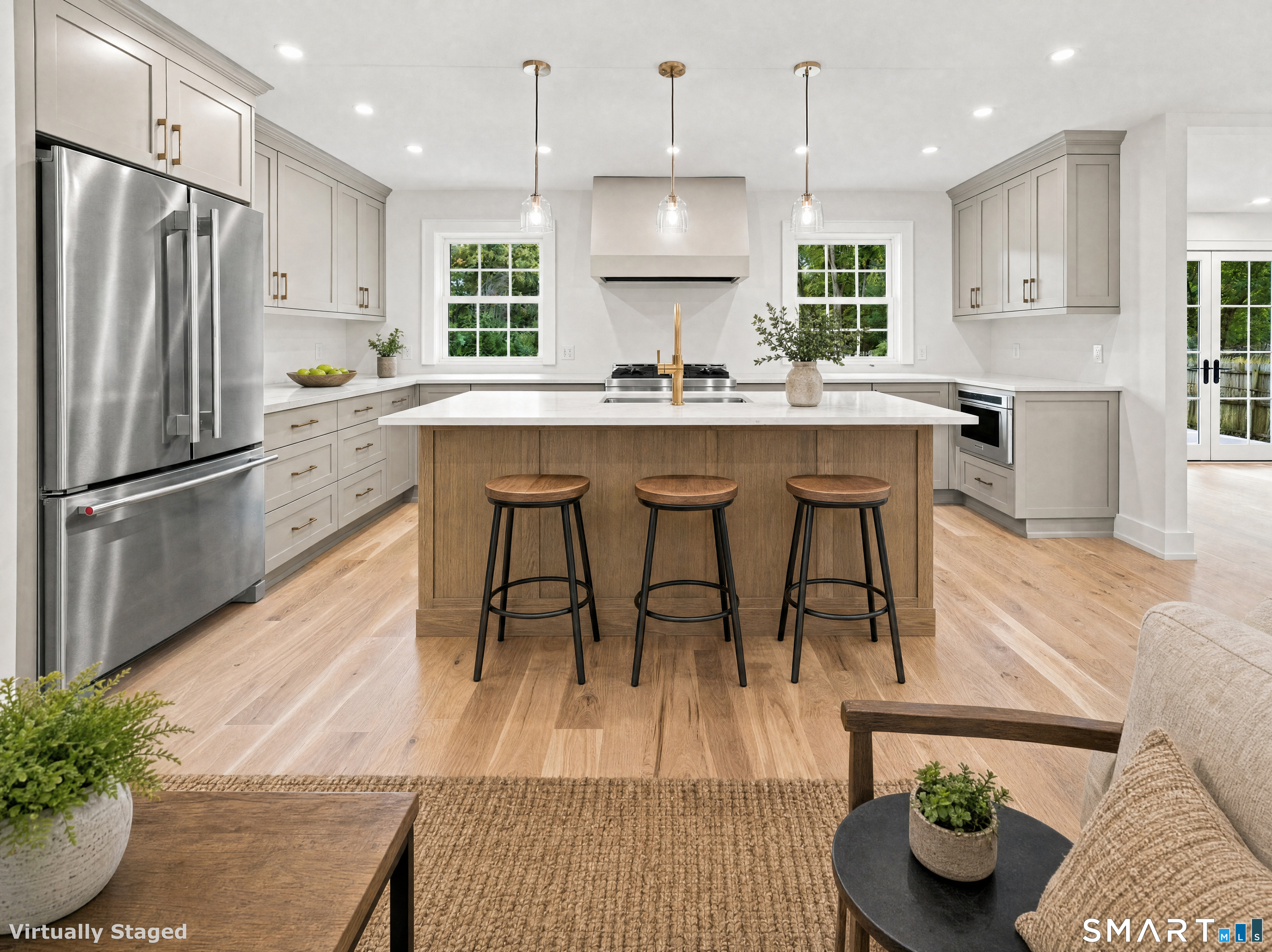 Bright staged kitchen with a wood island, three stools, stainless refrigerator, and white cabinetry.