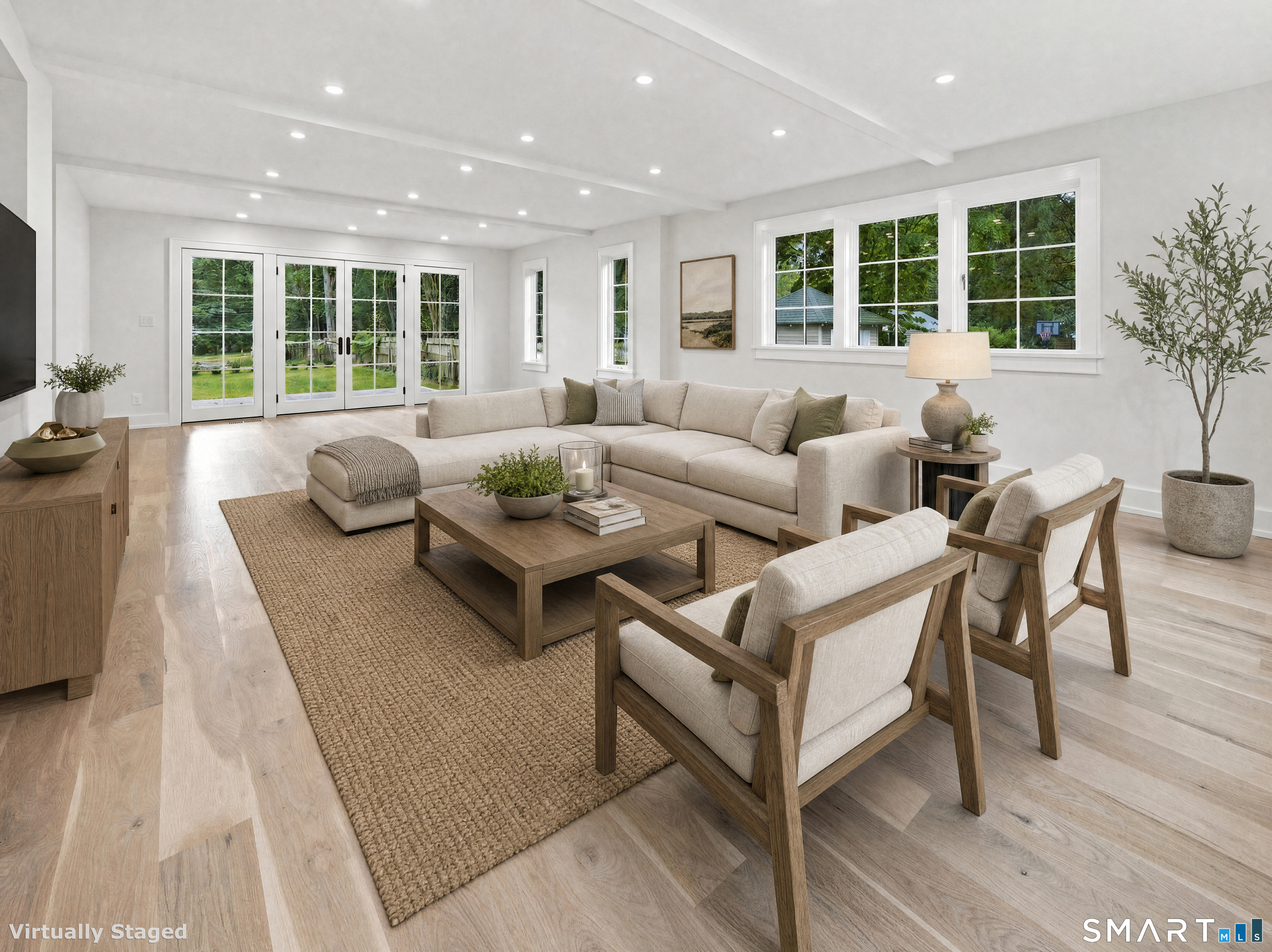 Virtually staged living room with a cream sectional, wood-framed chairs, and large windows overlooking greenery.