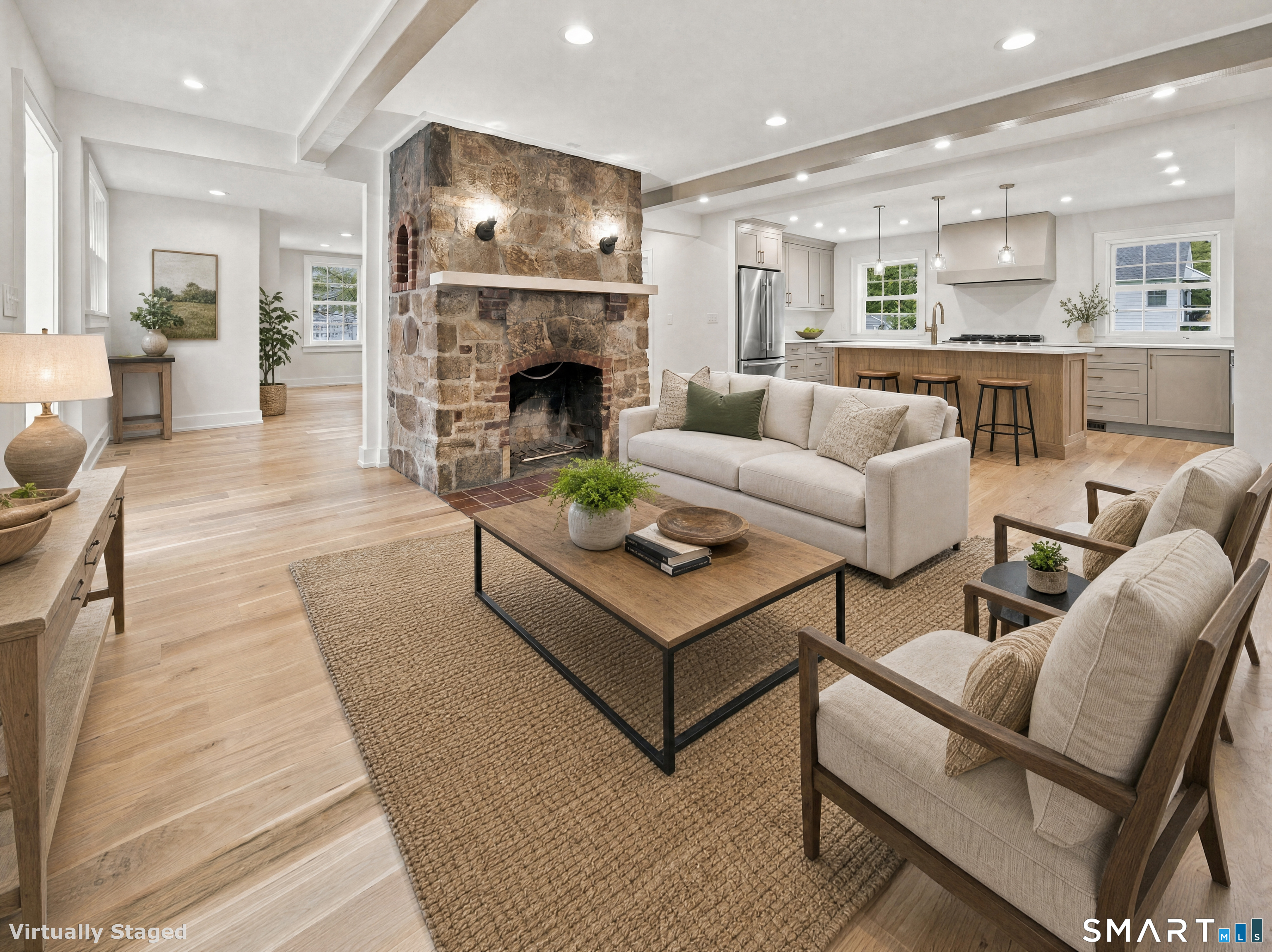 Open-plan living room and kitchen with a large stone fireplace and neutral furnishings.