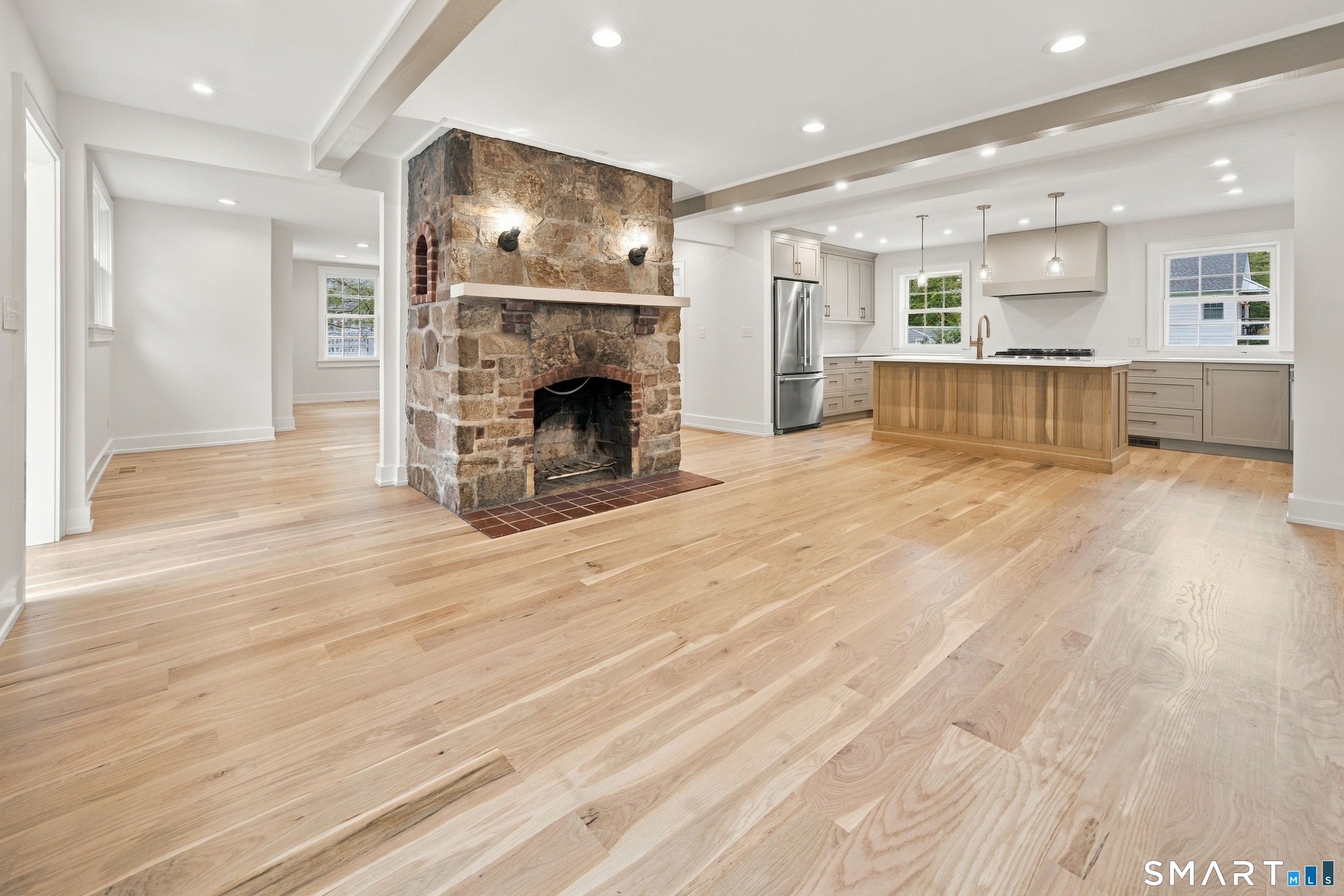 Open kitchen and living area with a large stone fireplace, wood island, and light hardwood floors.