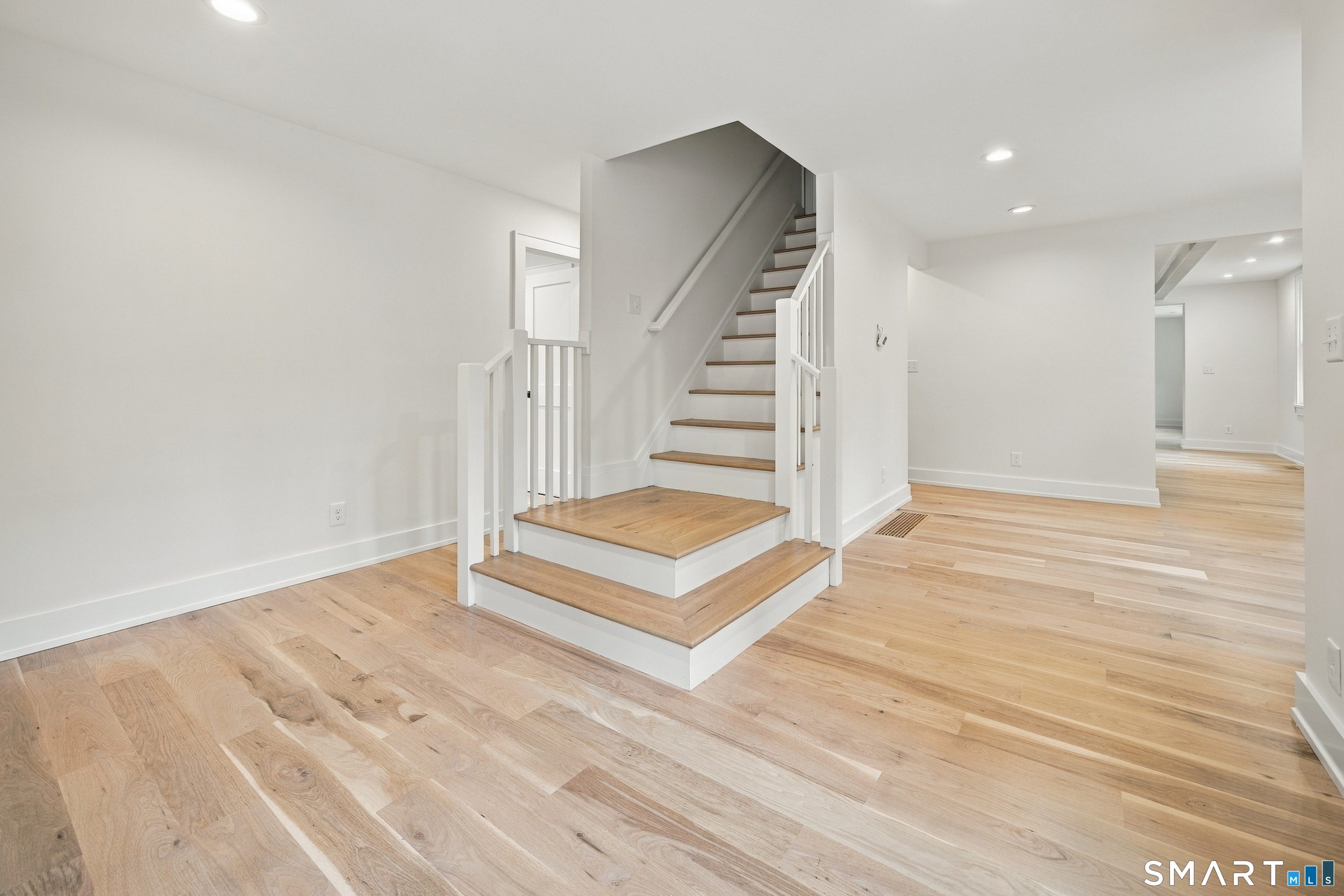 Central staircase with white railings and wood treads in a bright, vacant interior.