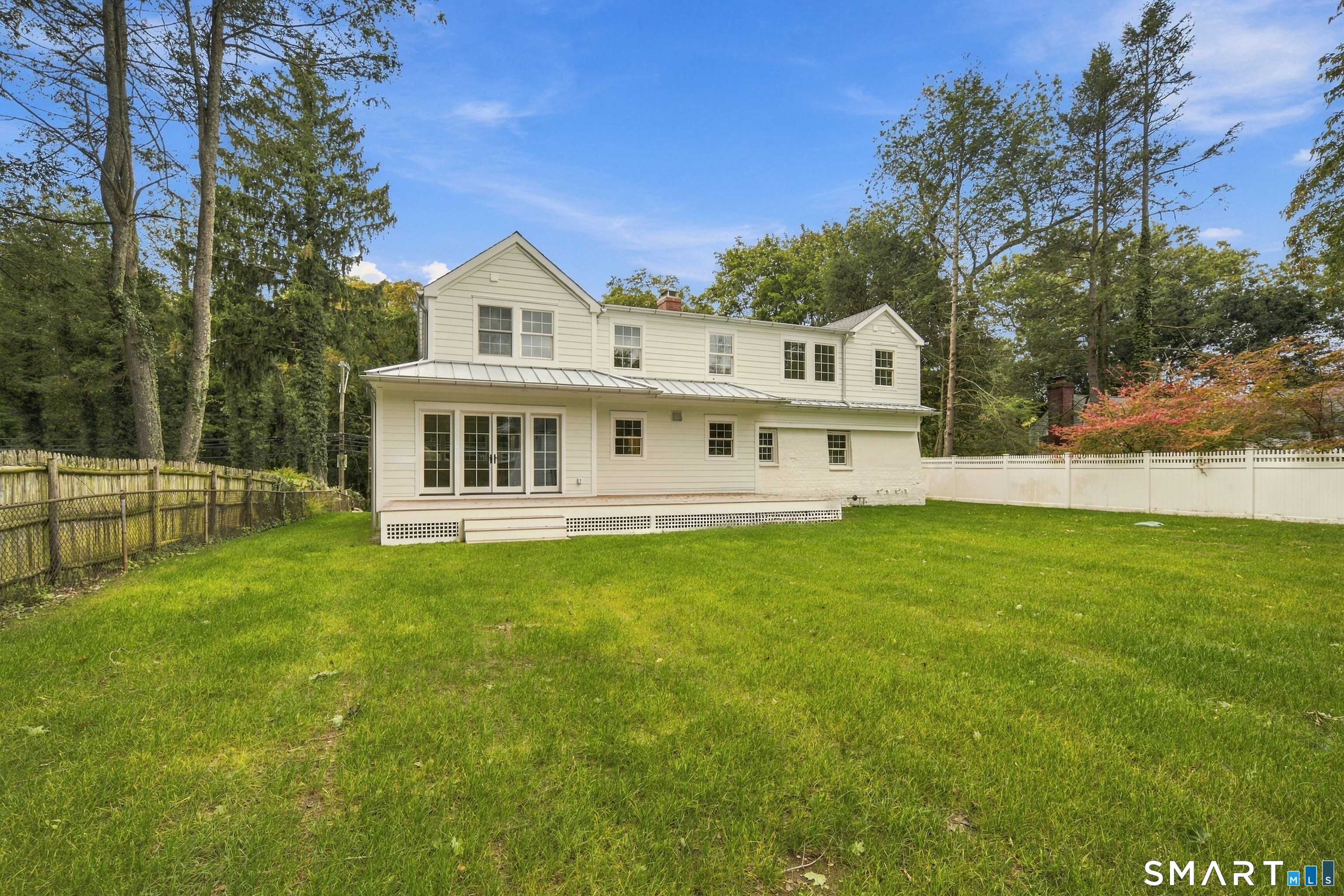 Rear exterior of a white two-story house overlooking a broad lawn, with mature trees and white fencing.