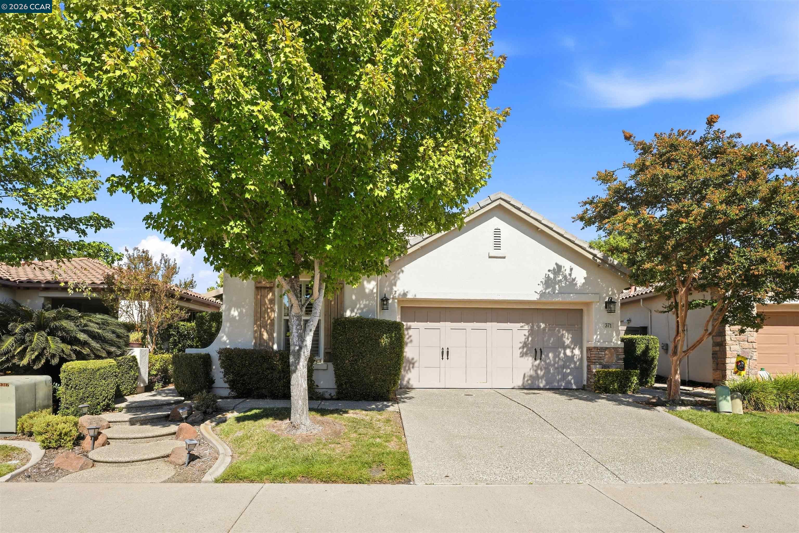 Suburban home with a two-car garage, broad driveway, and mature trees shading the front yard.
