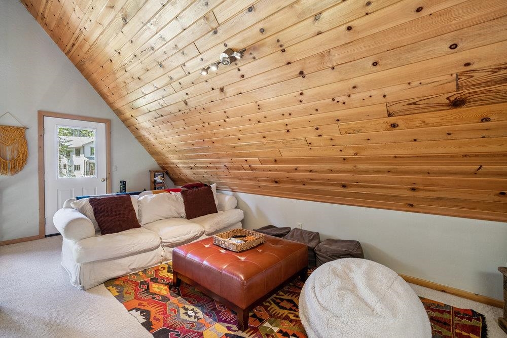 Living room with a sloped knotty-wood ceiling, white sofa, and colorful patterned rug.