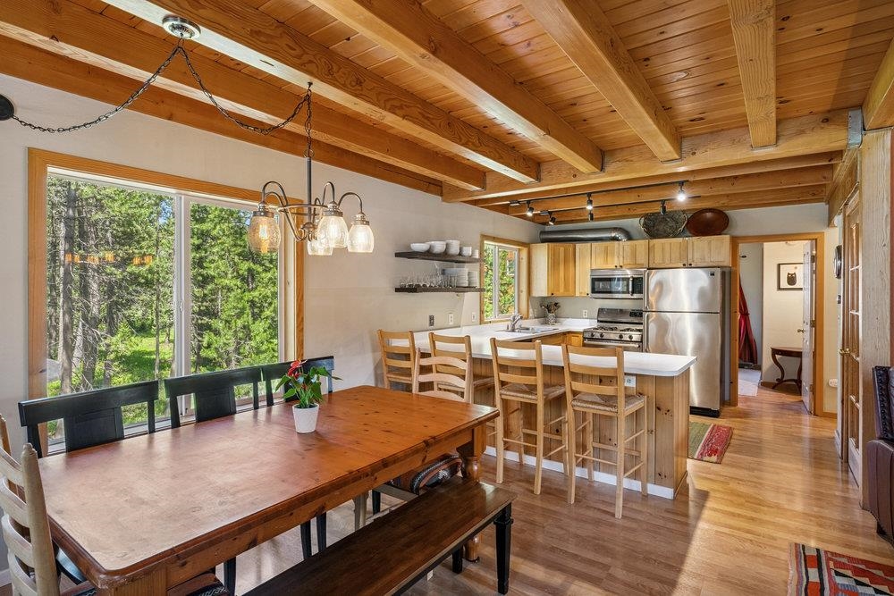 Open kitchen and dining area with exposed wood ceiling, breakfast bar, and forest views.