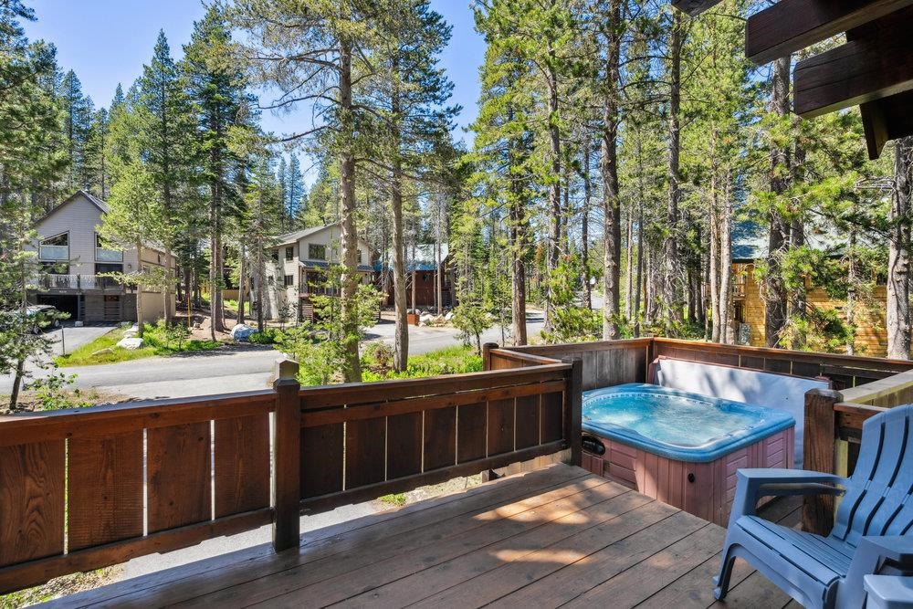 Wooden deck with a hot tub and blue chairs, surrounded by tall pine trees.