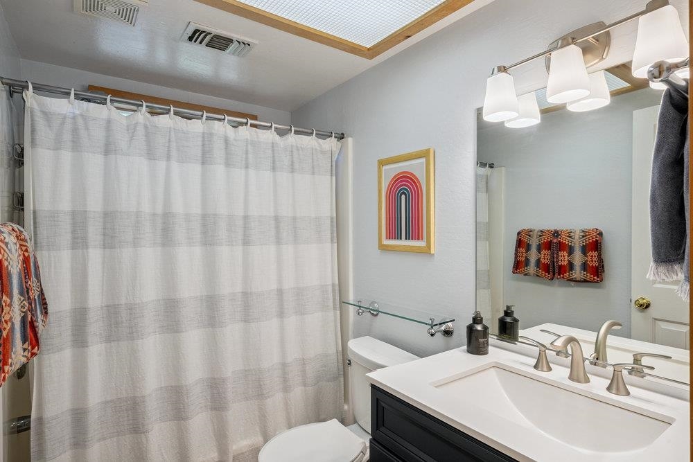 Bathroom with a striped shower curtain, dark vanity, wide sink, and large mirror.