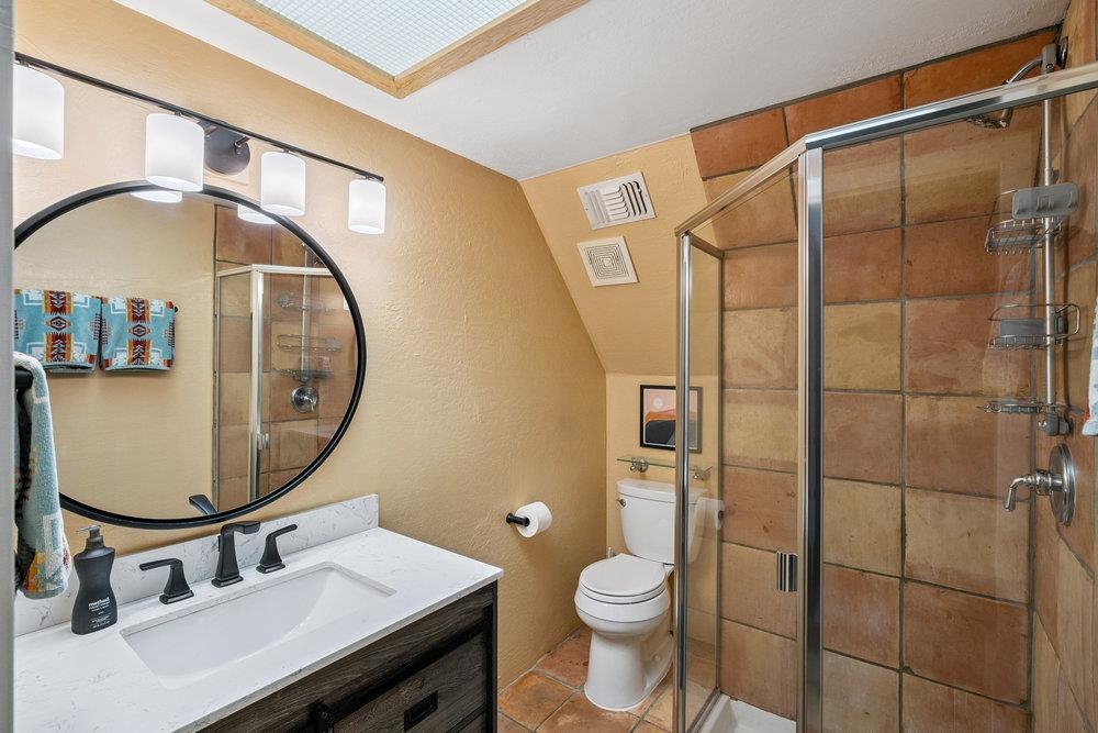 Bathroom with a round mirror, tiled glass shower, and skylight.