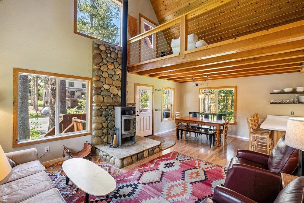 Living room with a stone fireplace, vaulted wood ceiling, loft, and colorful geometric rug.