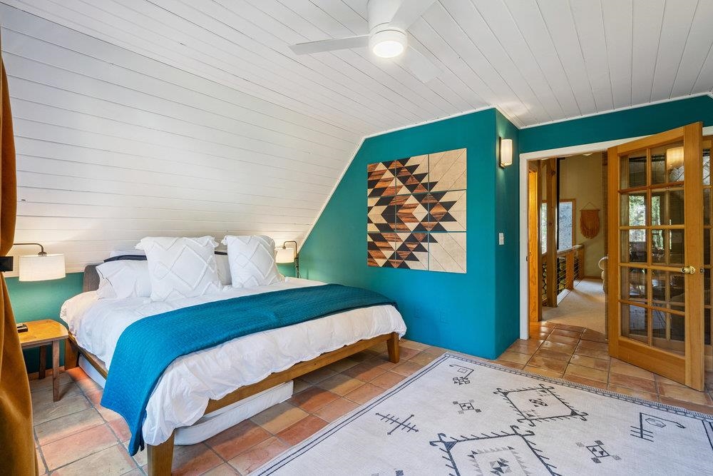 Furnished bedroom with a teal accent wall, geometric artwork, and wooden French doors.