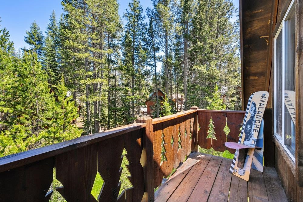 Wooden balcony overlooking pine trees, with a snowboard leaning beside the railing.