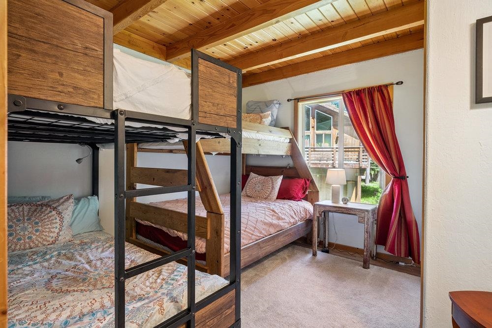 Bedroom with wooden bunk beds, a vaulted wood ceiling, and red curtains beside a window.