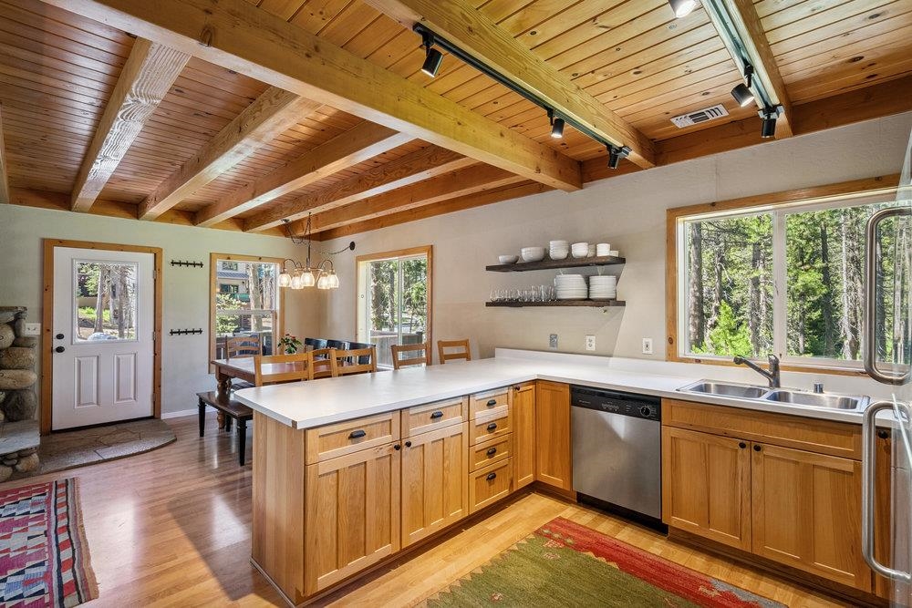 Kitchen with a large white island, exposed wood beams, and windows overlooking trees.