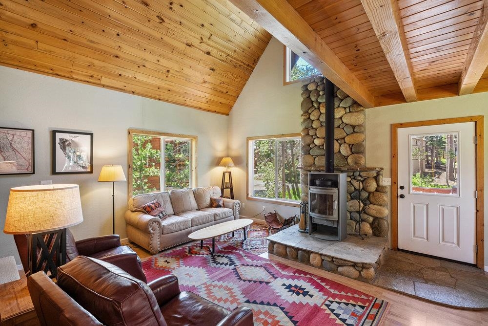 Living room with a vaulted wood ceiling, stone fireplace, leather seating, and a colorful rug.