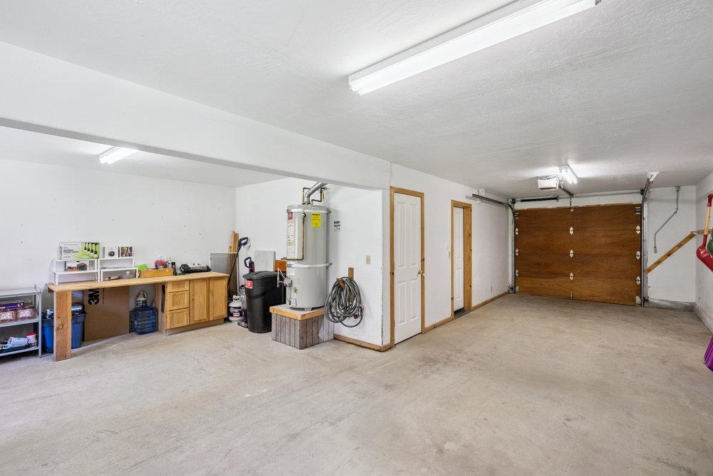 Spacious garage with a wooden overhead door, water heater, and workbench along the wall.
