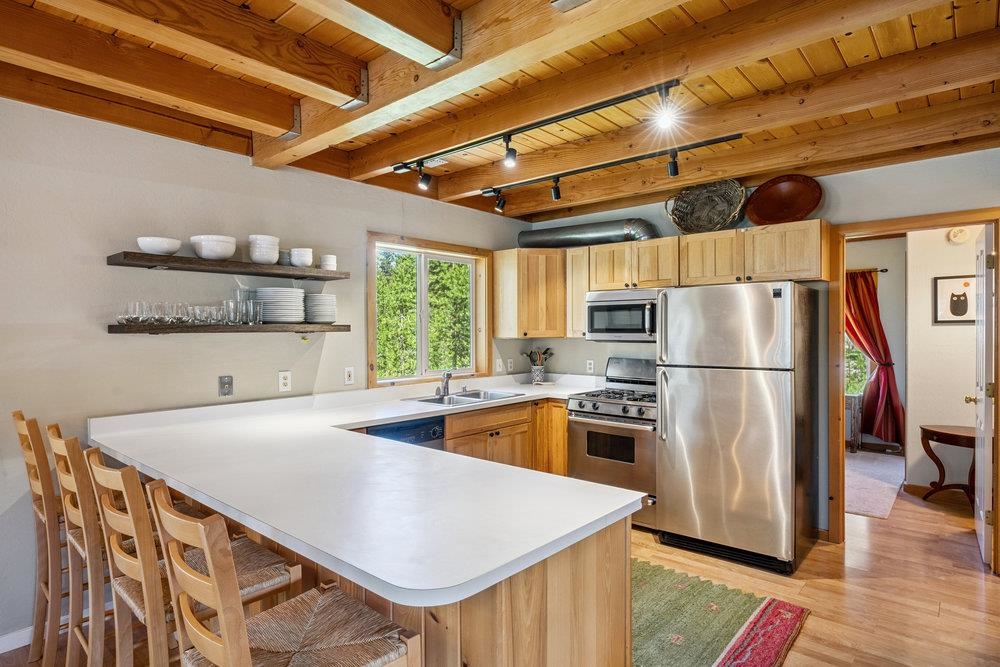 Kitchen with a white breakfast bar, wooden chairs, stainless steel appliances, and exposed ceiling beams.