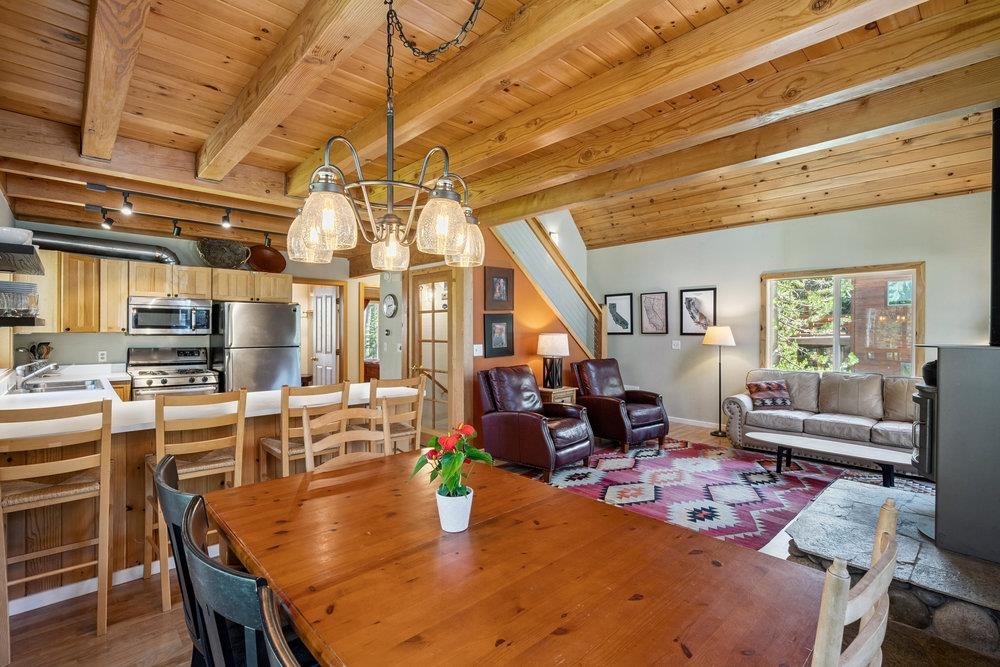 Open-plan living area with a vaulted wood ceiling, dining table, kitchen, and sitting area.