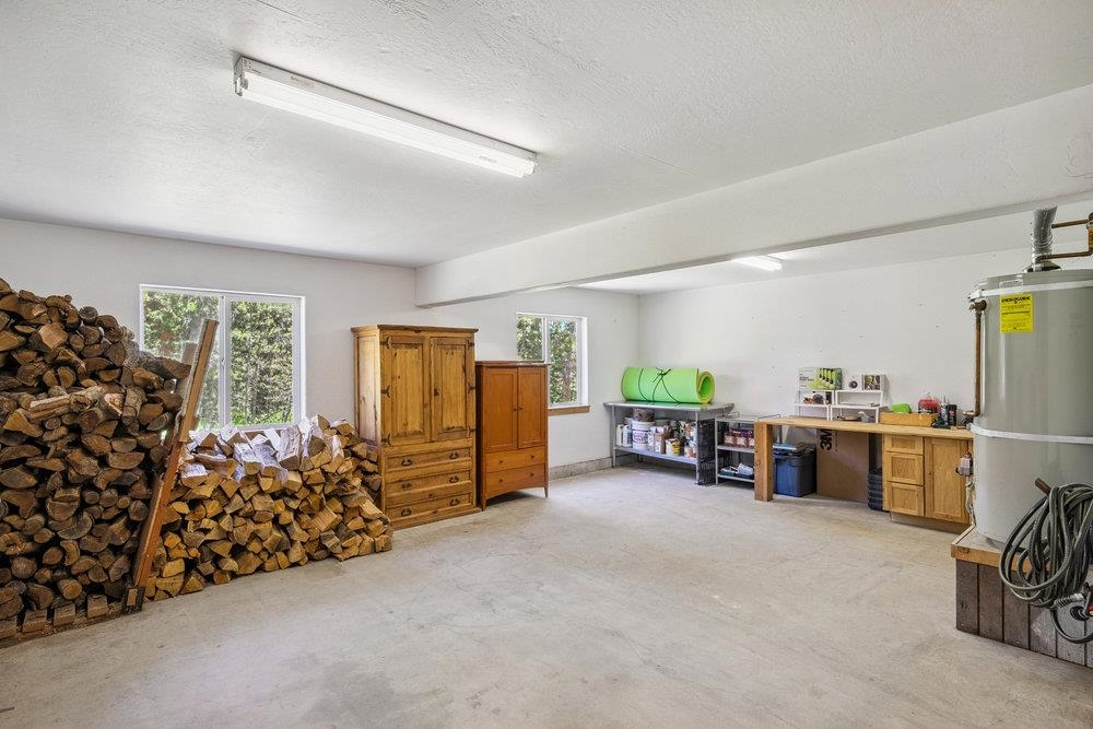 Garage with stacked firewood, wooden dressers, shelving, and a workbench.