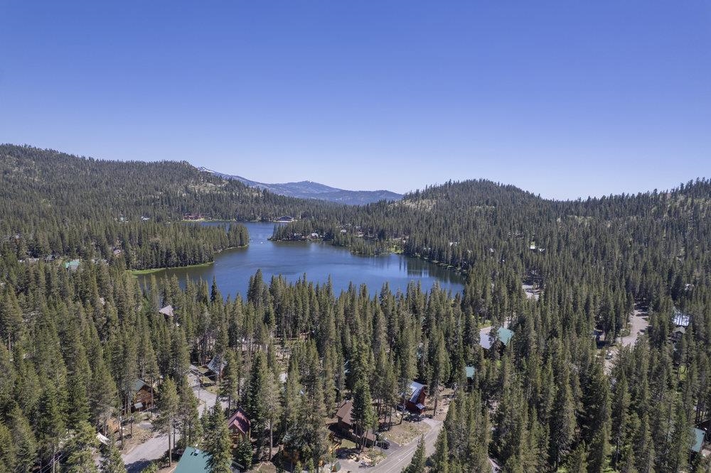 Aerial view of a forested neighborhood and lake, with mountain ridges in the distance.