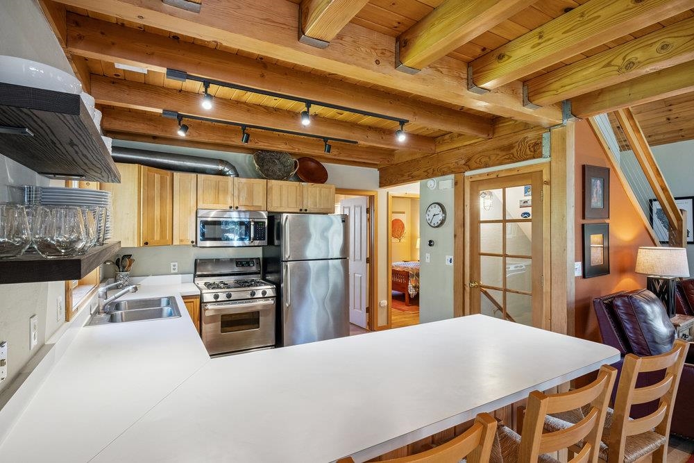 Kitchen with exposed timber beams, stainless steel appliances, and a broad white island with seating.