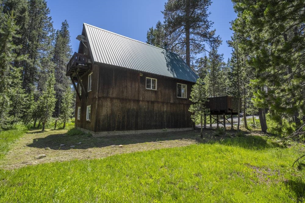 Dark wood cabin with a steep metal roof and raised decks among pine trees.