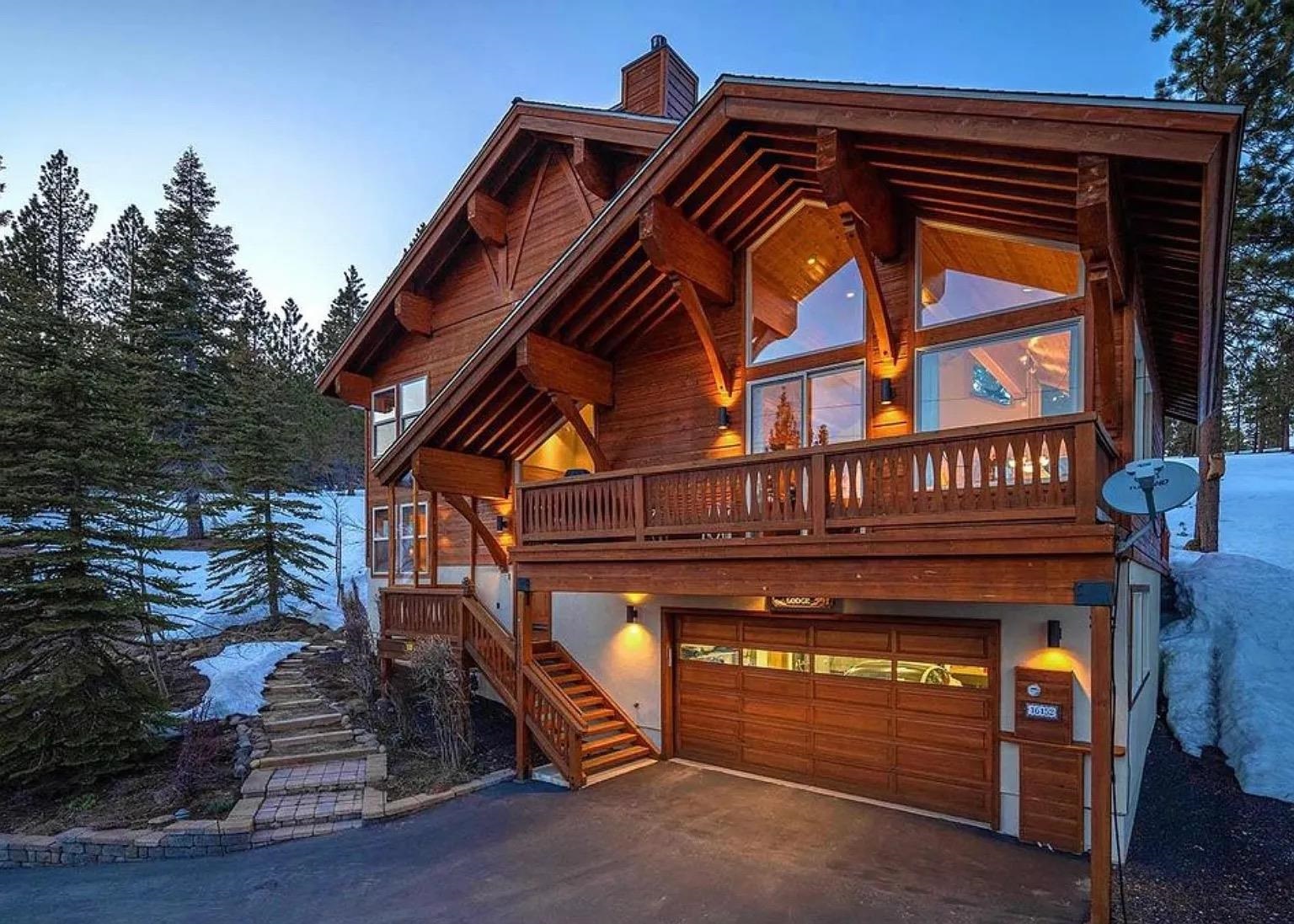 Timber mountain home with a covered balcony and double garage among snow-covered evergreens.