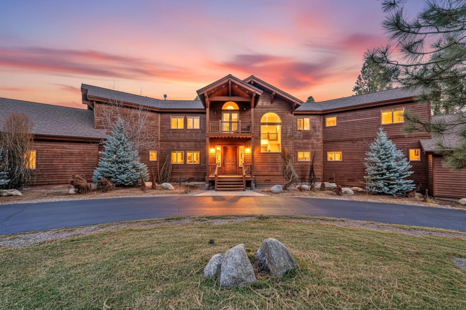 Large wooden home with a central gabled entrance and glowing windows at sunset.